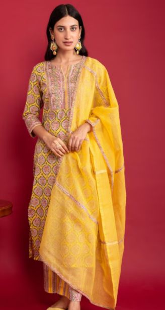 Best salwar suit in kunnamkulam-A woman wearing a printed salwar suit with a yellow dupatta stands against a red background, accessorized with statement earrings.